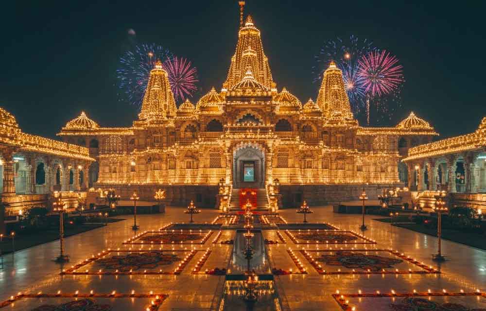 The exterior of a large, ornate Indian temple beautifully illuminated at night for Diwali. The entire structure is covered in thousands of bright string lights and hundreds of glowing clay diyas placed on the steps and ledges