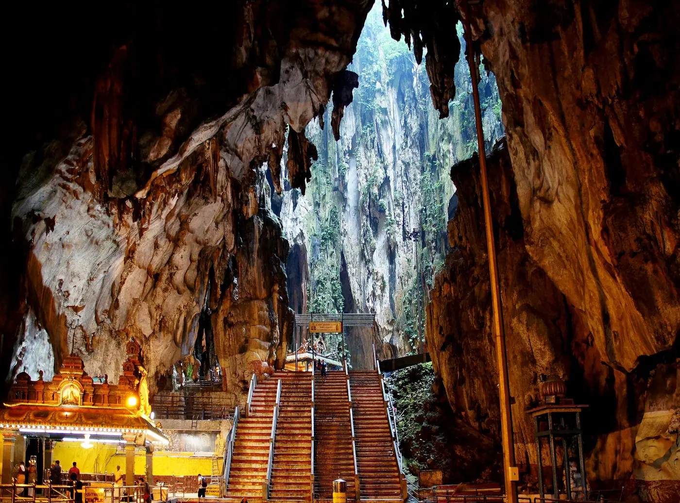 Inside the Temple Cave at Batu Caves, with the staircase rising towards the cave opening and a lit shrine at left