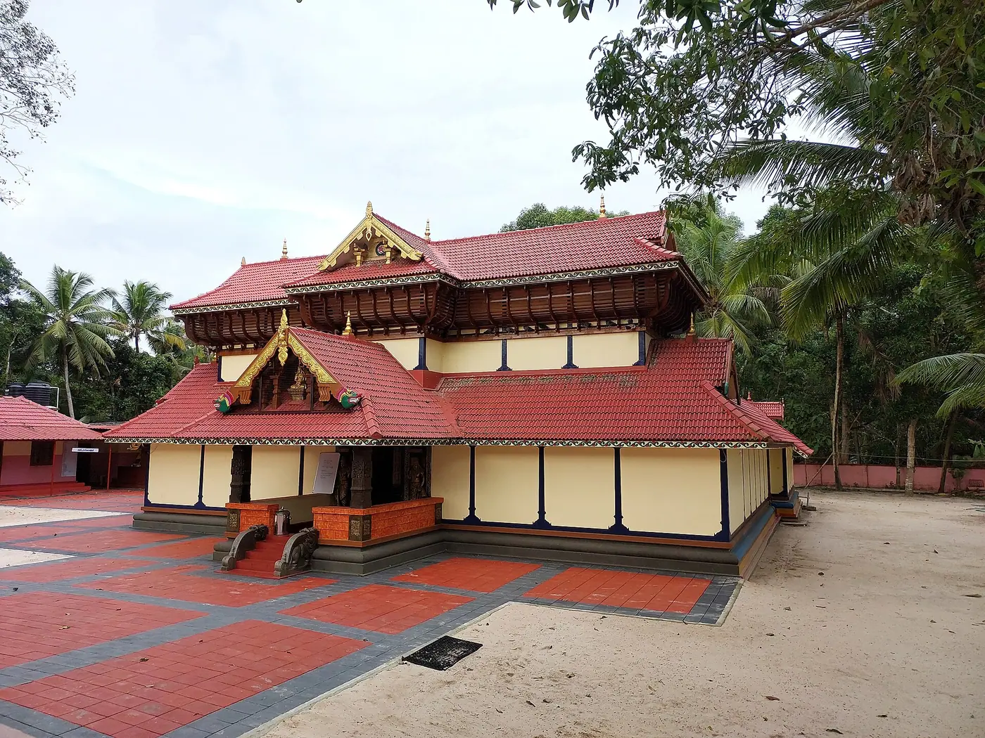 Red-tiled Padmapuram Adithya Temple in Kerala, surrounded by coconut palms